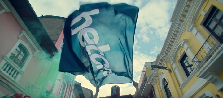 Aficionado ondea una bandera azul con el logotipo de Betcris en una calle de fachadas coloniales